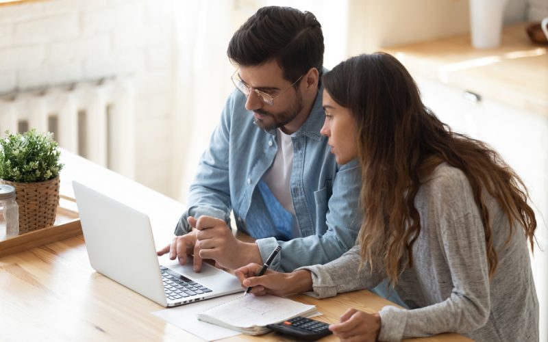 Busy,Serious,Couple,Sit,In,Kitchen,Look,At,Laptop,Screen